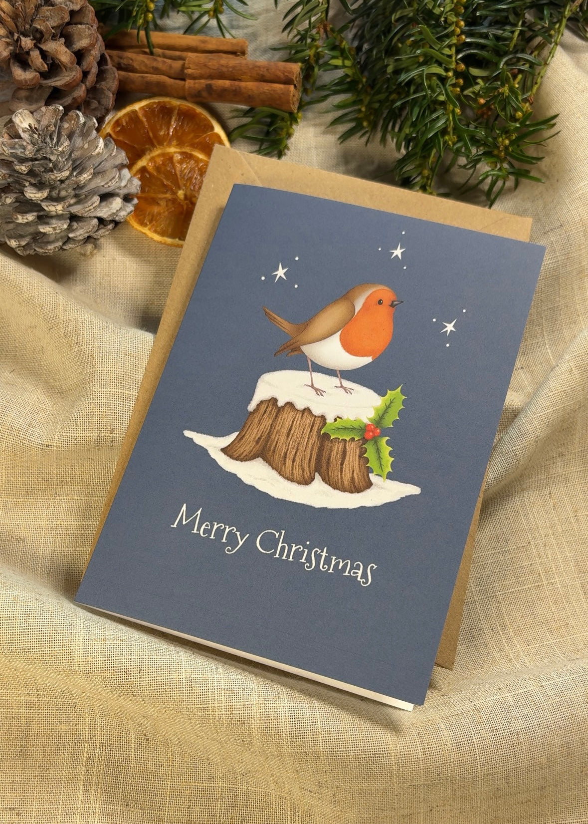 Christmas card with a robin on a tree stump illustration, surrounded by festive decorations.